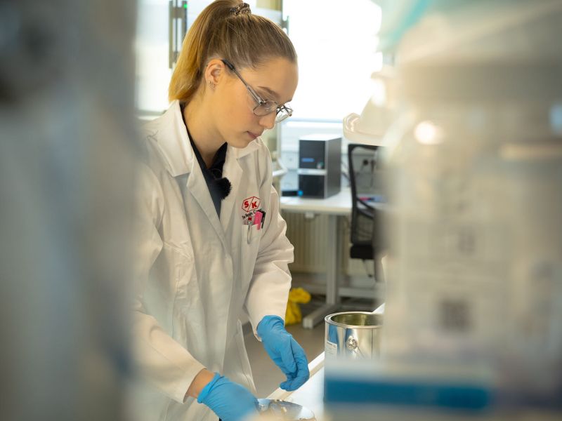 Im Synthopol Chemielabor eine Frau mit weißem Kittel und Handschuhen